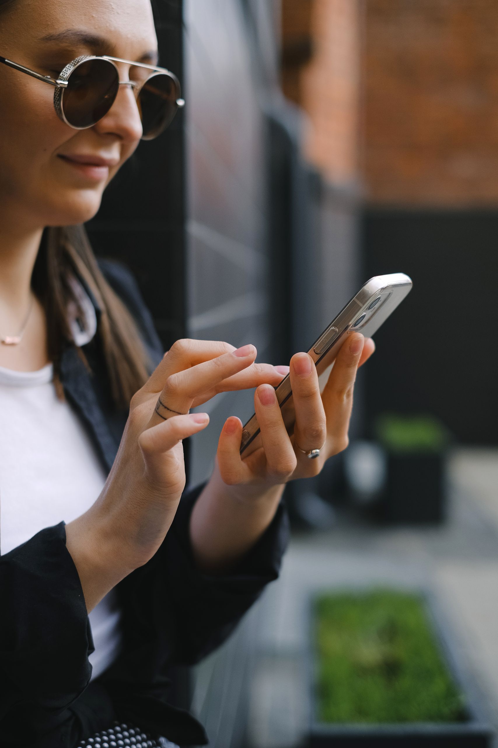 Woman holding smartphone, using it outdoors on a sunny day, wearing sunglasses.
