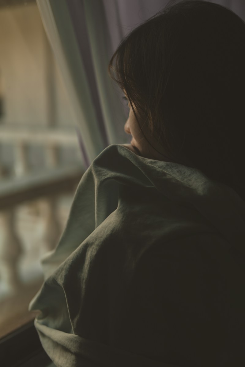 A person looking out a window draped in a soft green fabric