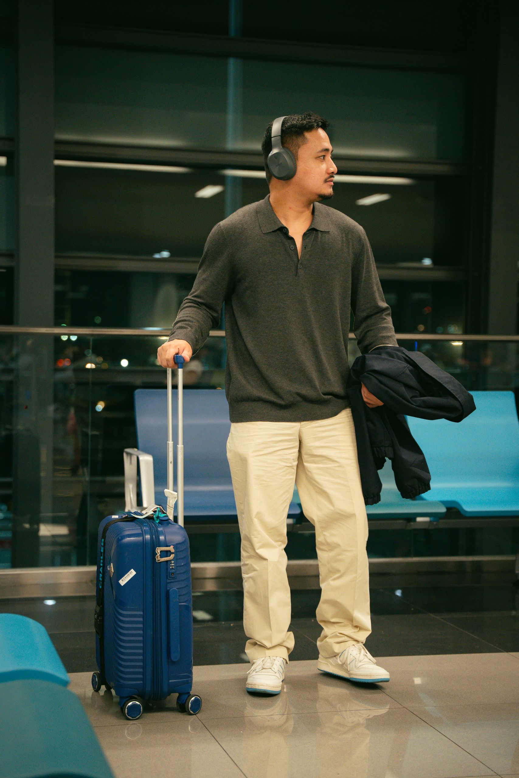 Young man with headphones and suitcase waiting at airport terminal.