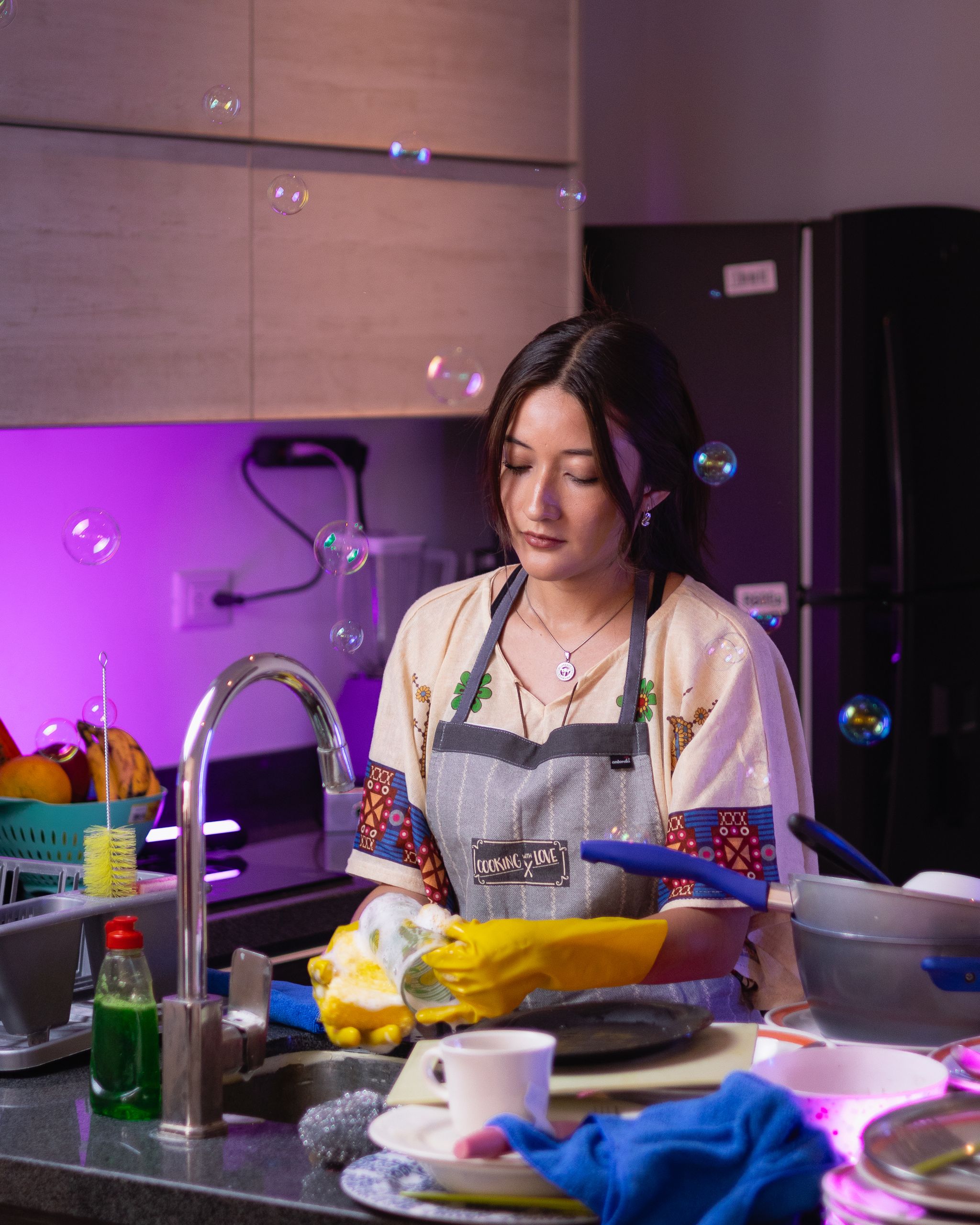 Young woman washing dishes with soap bubbles in a modern kitchen setting.