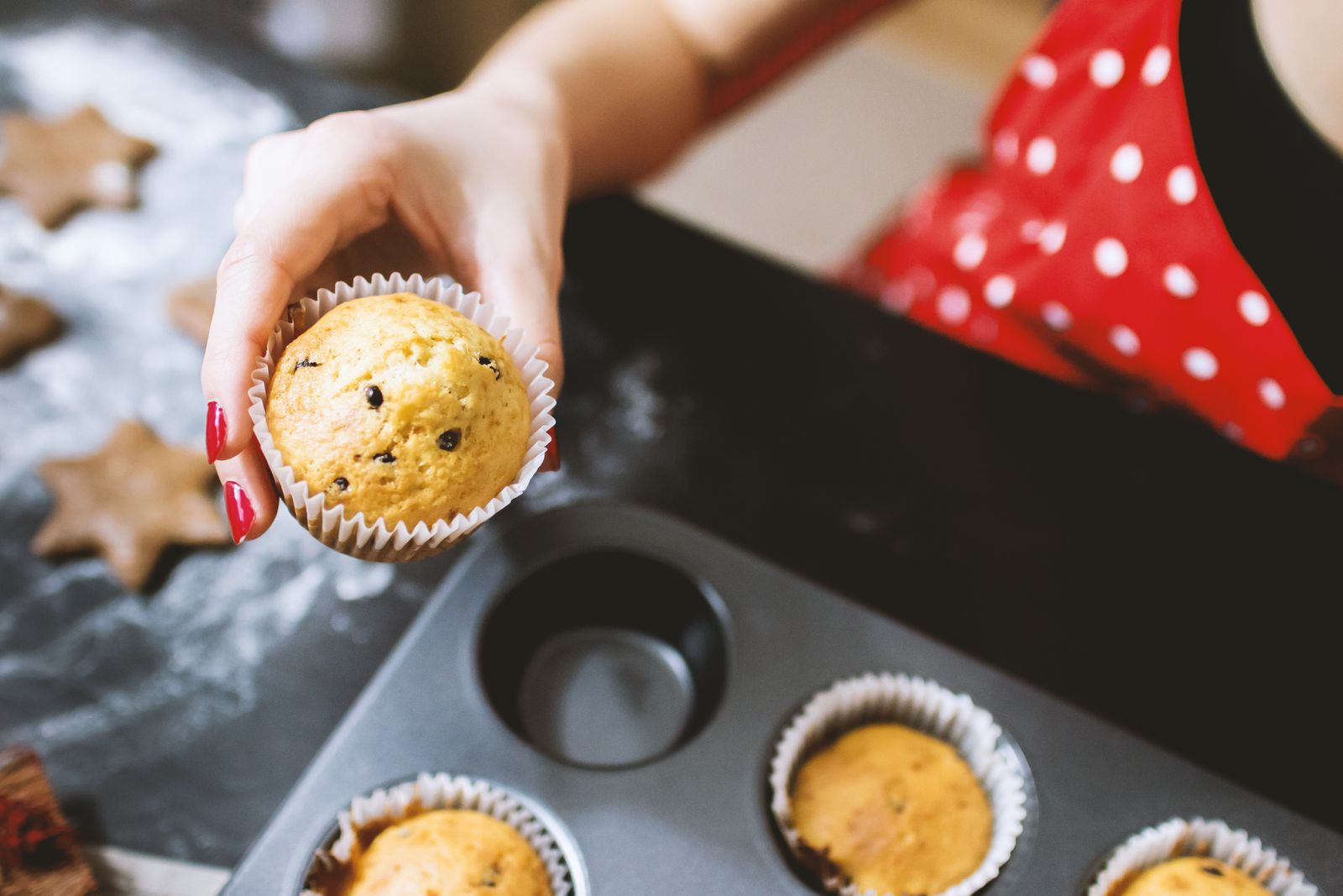 A person holding a chocolate chip cupcake fresh from the oven in a kitchen setting.