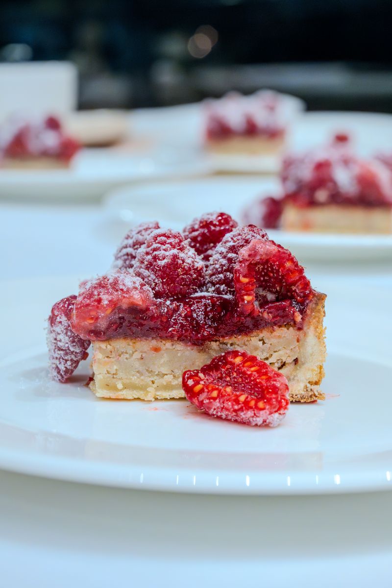 A mouthwatering raspberry tart topped with powdered sugar, perfect for dessert lovers.