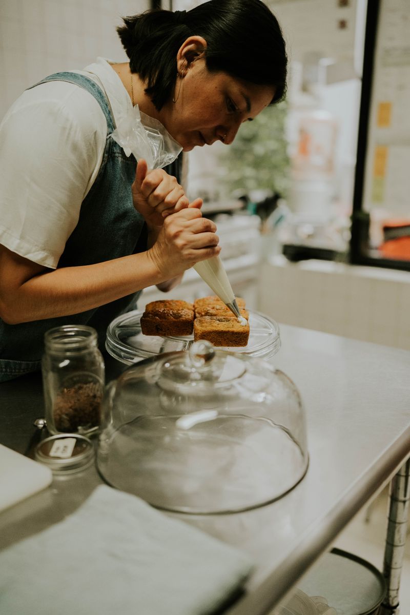A focused pastry chef decorates cakes with precision in a cozy kitchen setting.