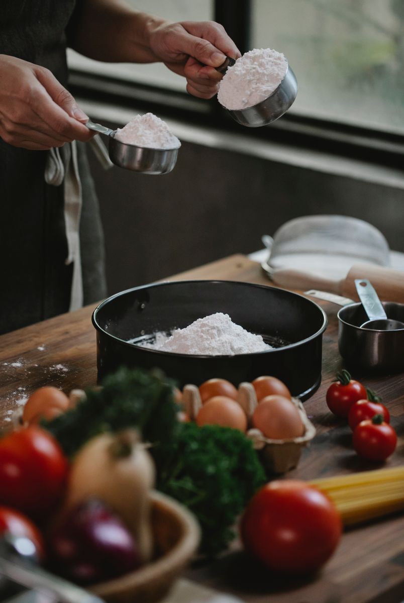 Crop anonymous chef in apron preparing ingredients for adding to flour in baking form at kitchen