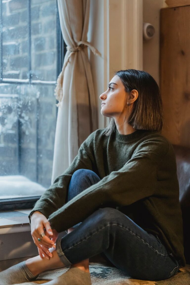 Side view of young female sitting in solitude and thoughtfully looking in window