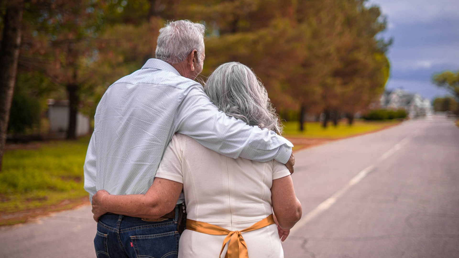 An older couple walking arm in arm down a road. Photo by Hector Reyes on Unsplash.