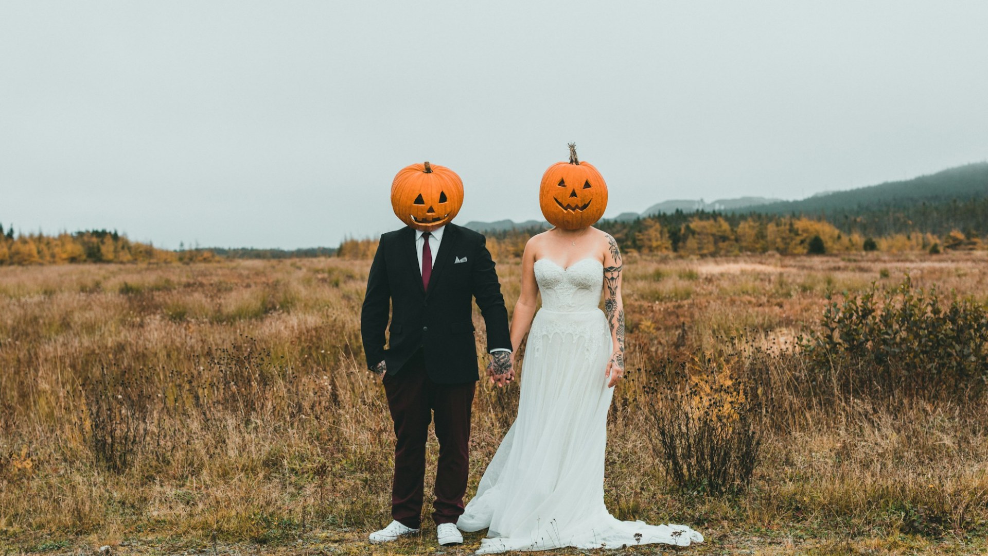 A couple wearing pumpkin heads in a field. Photo by Jonathan Cooper on Unsplash.
