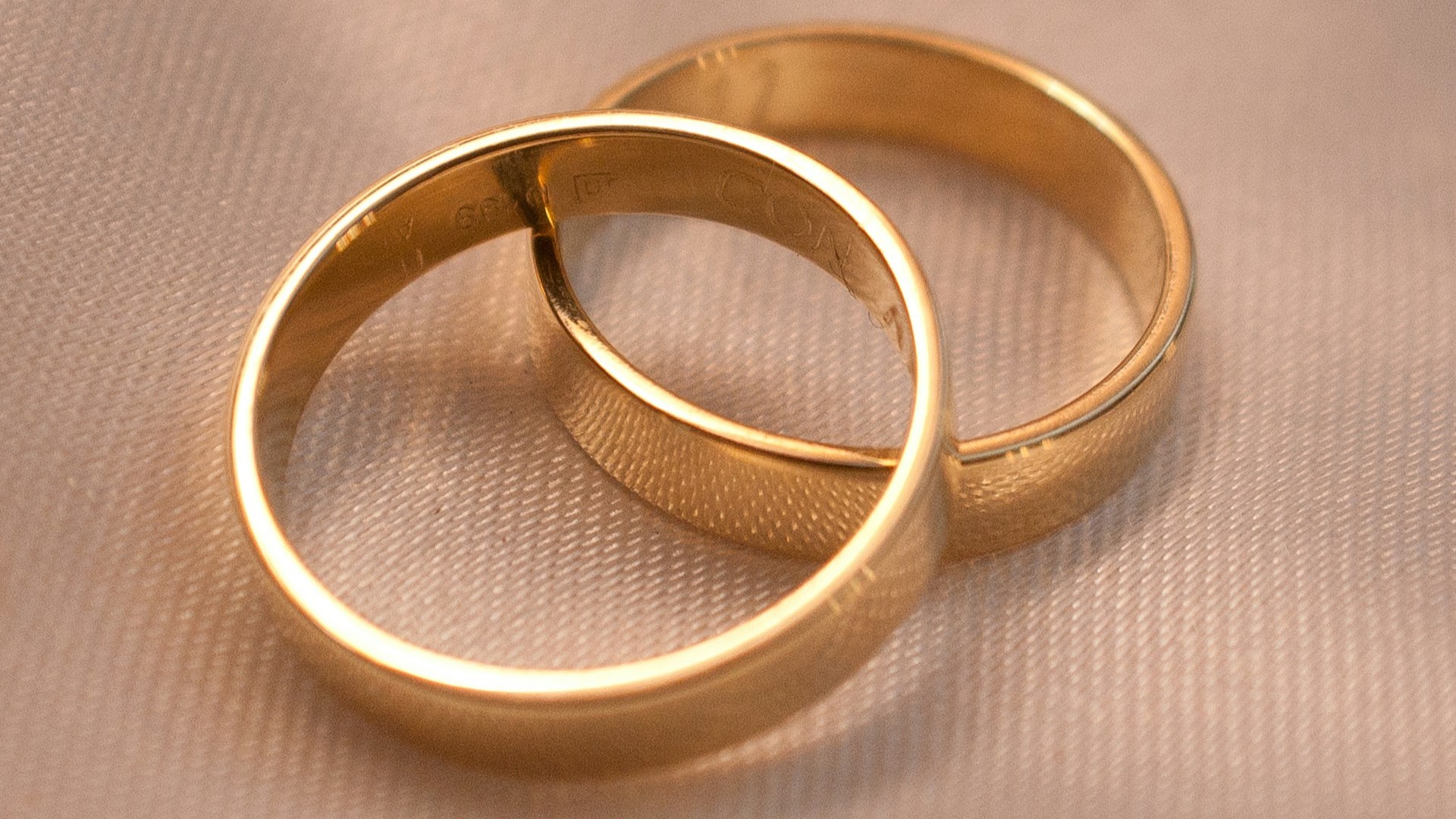 Unsplash photo by Mariano Rivas showing two linked gold wedding bands on cream fabric