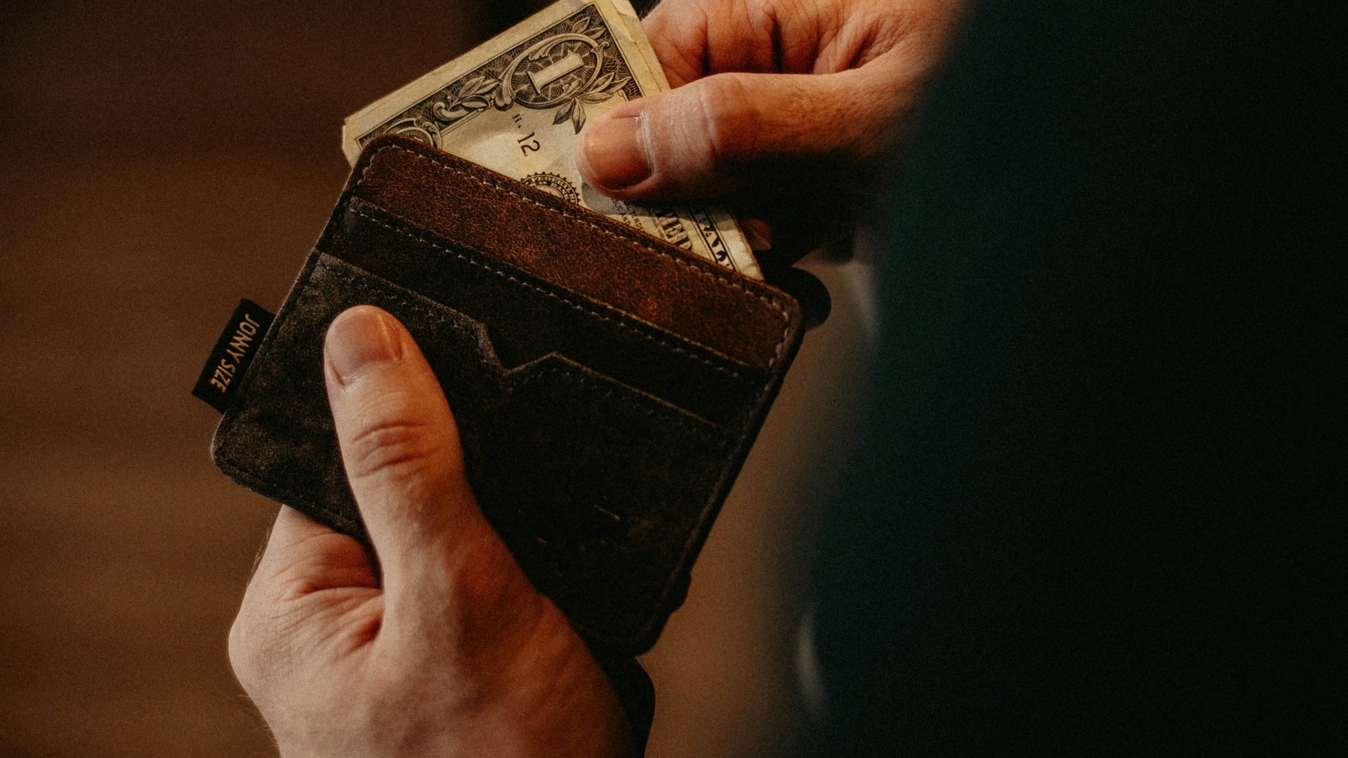 Unsplash photo by Allef Vinicius showing a person's hands taking a US one-dollar bill from a wallet