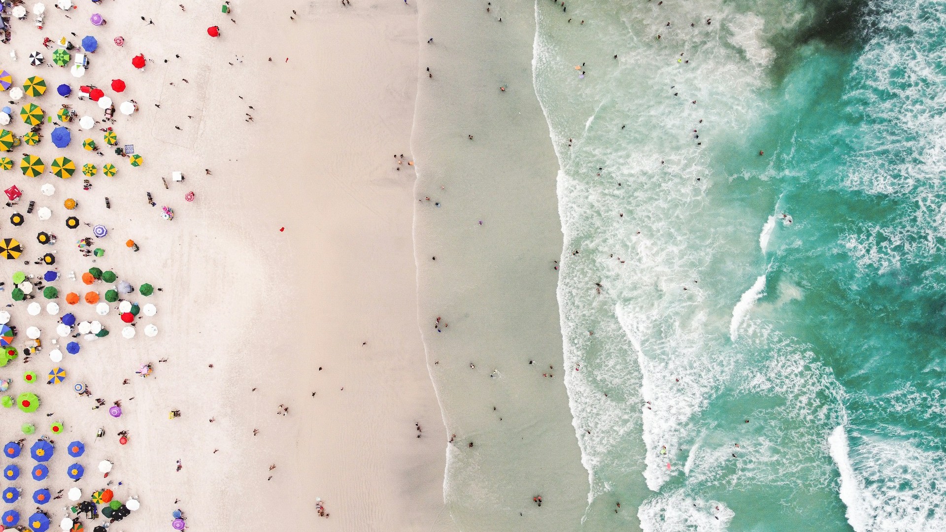 Unsplash photo by Pedro Oliveira showing an aerial view of a crowded beach with colorful umbrellas and waves